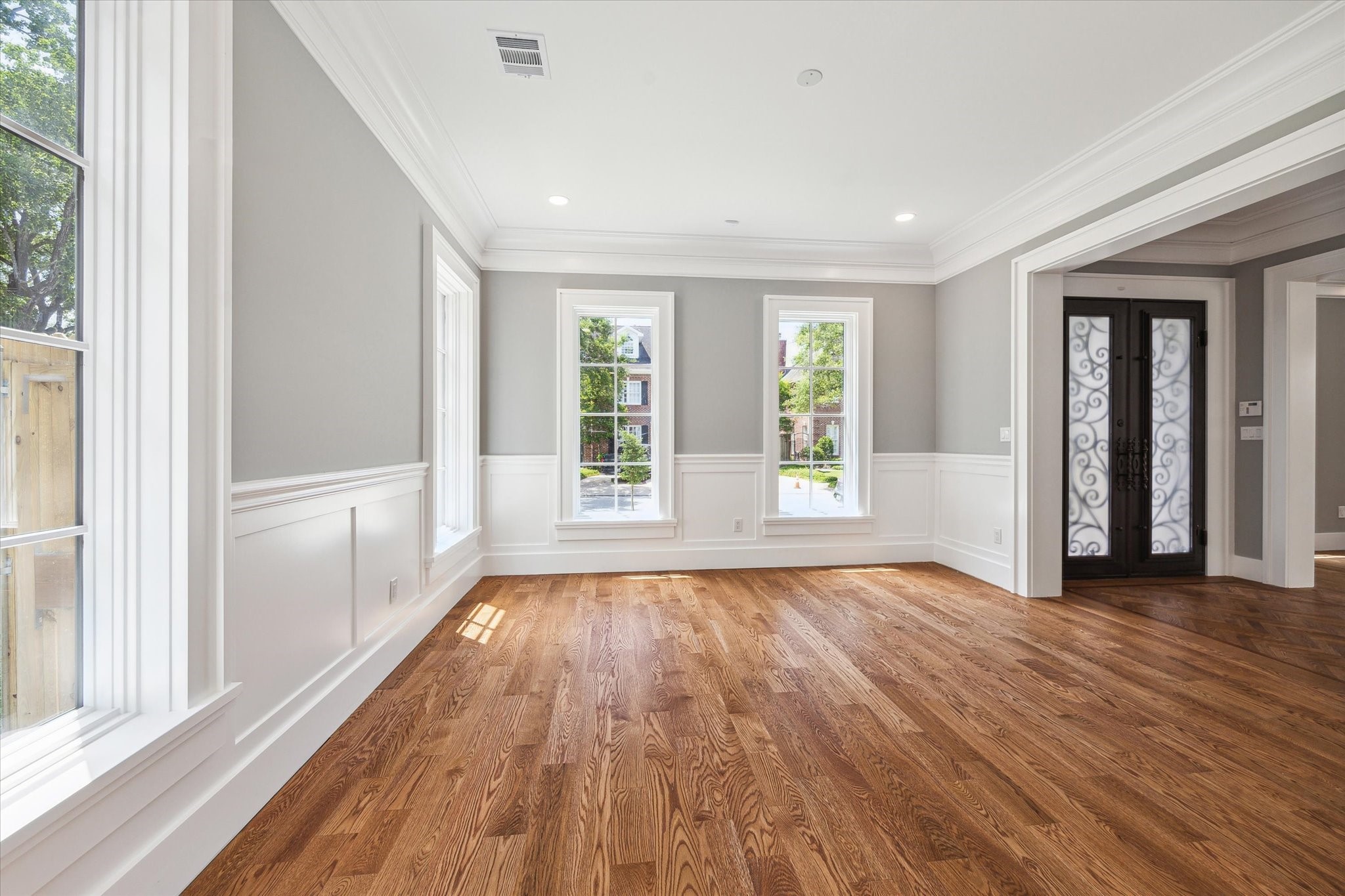 2216 Tangley Street Houston, TX 77005 - Photo 30 of 44 This photo shows the bright and spacious dining room with hardwood floors, large windows, and elegant crown molding. The neutral gray walls and white wainscoting add a touch of sophistication, and the decorative front door enhances the entryway as you look from the dining room.