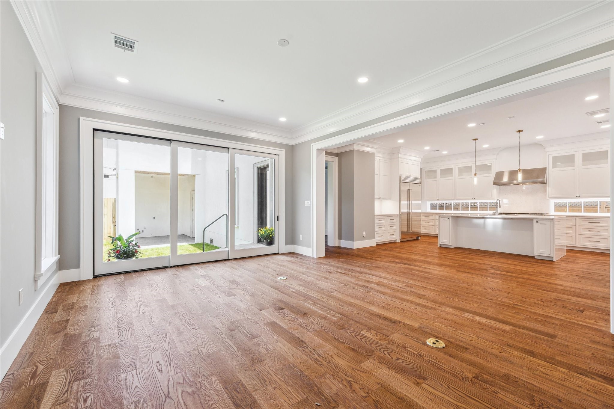 2216 Tangley Street Houston, TX 77005 - Photo 35 of 44 This photo showcases a spacious open-concept living area with hardwood floors, large sliding glass doors leading to the outdoor space, and a modern kitchen featuring an island and ample cabinetry. The area is well-lit with recessed lighting and pendant lights above the island.