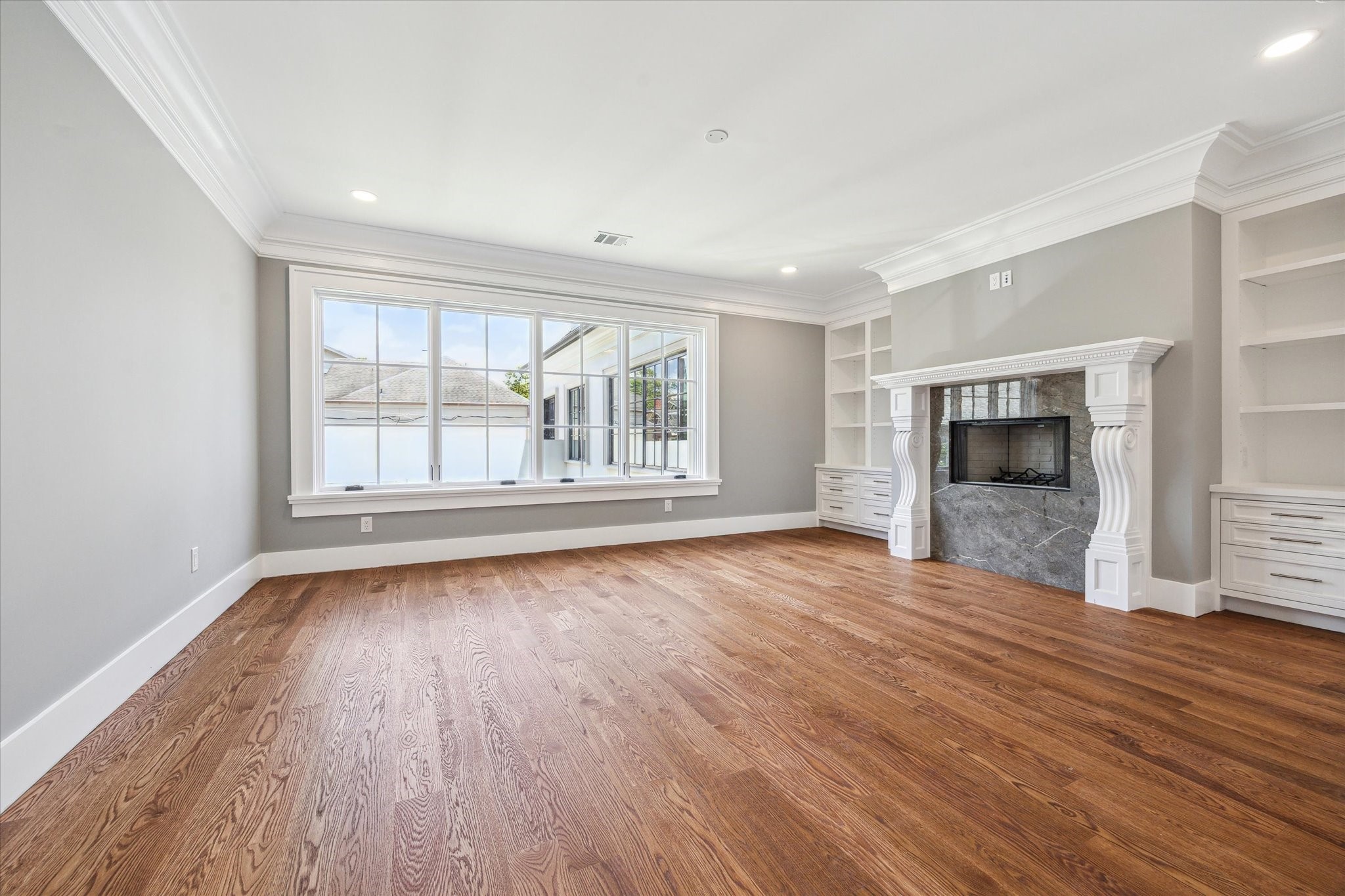 2216 Tangley Street Houston, TX 77005 - Photo 37 of 44 This view of the primary bedroom with hardwood floors, highlights the large windows, and stylish fireplace flanked by built-in shelves and opening to the luxurious primary bath.