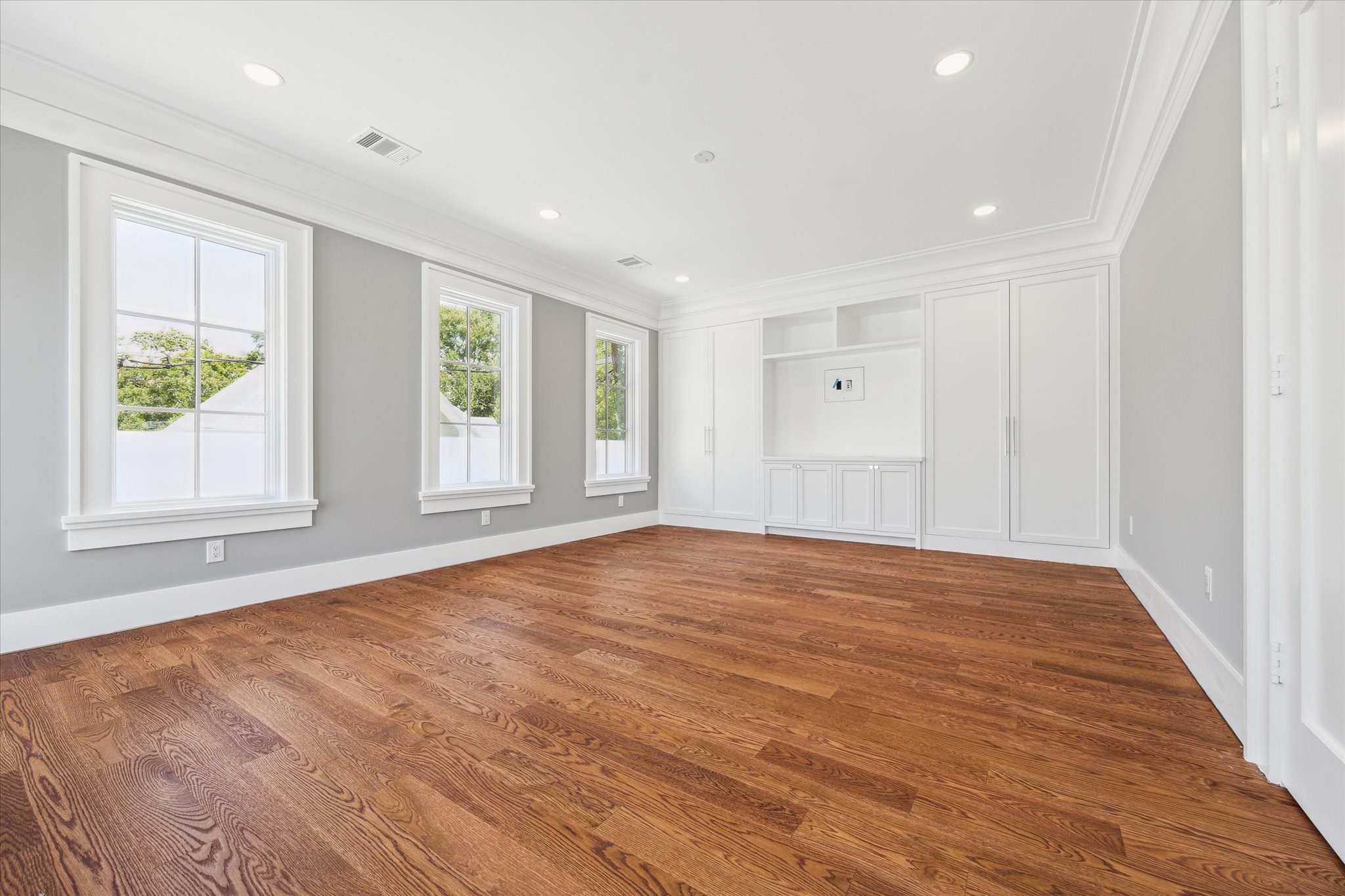 2216 Tangley Street Houston, TX 77005 - Photo 40 of 44 Another view of this 2nd floor bedroom that features hardwood floors, abundant natural light from three large windows, and built-in white cabinetry for storage. The neutral gray walls and recessed lighting create a modern and inviting atmosphere. This is the room that opens to the balcony.