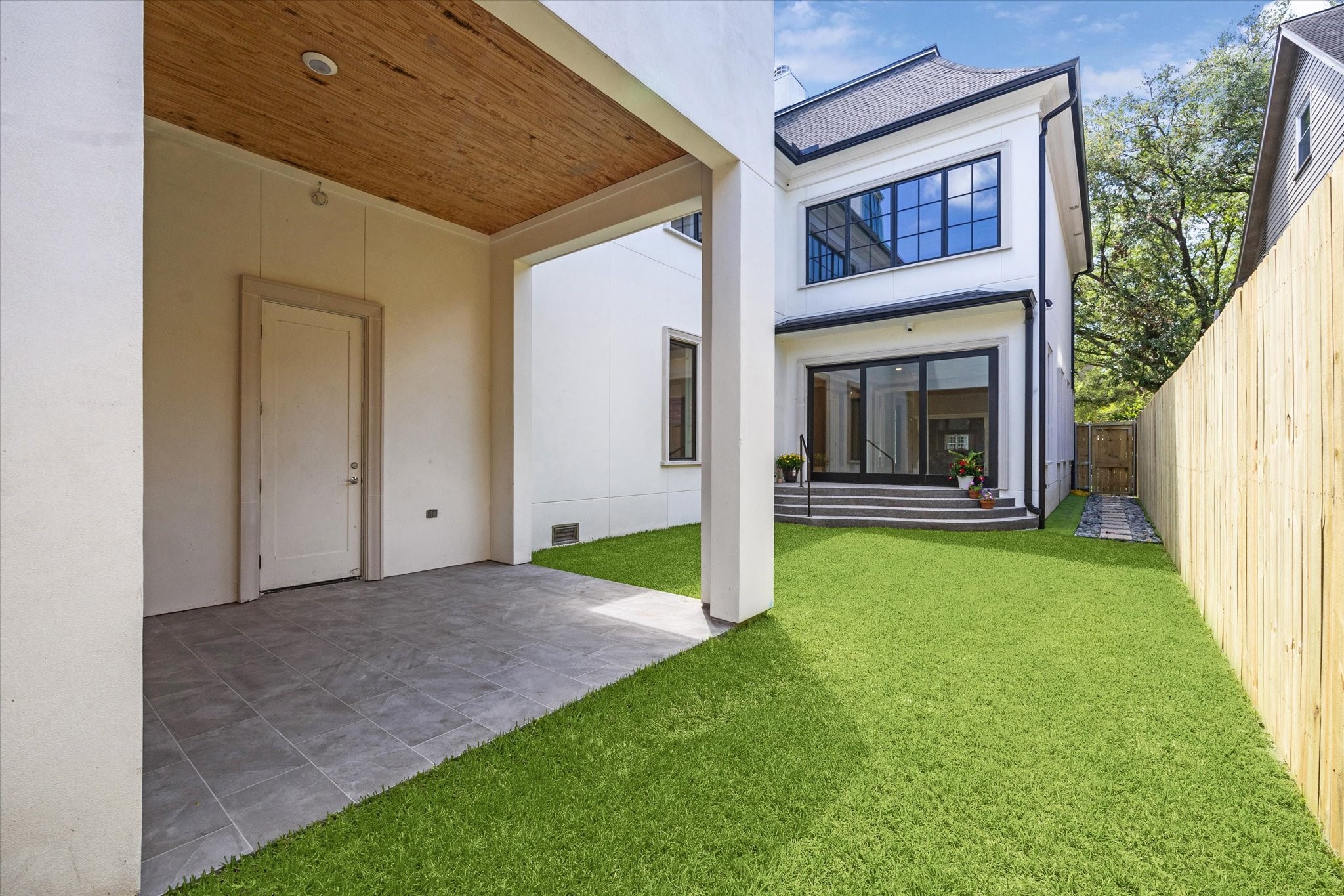2216 Tangley Street Houston, TX 77005 - Photo 44 of 44 Another view of the new construction, three story home with a clean white exterior, featuring a covered patio, lush green lawn, and a wooden fence for privacy. Large windows and a sliding door enhance natural light.