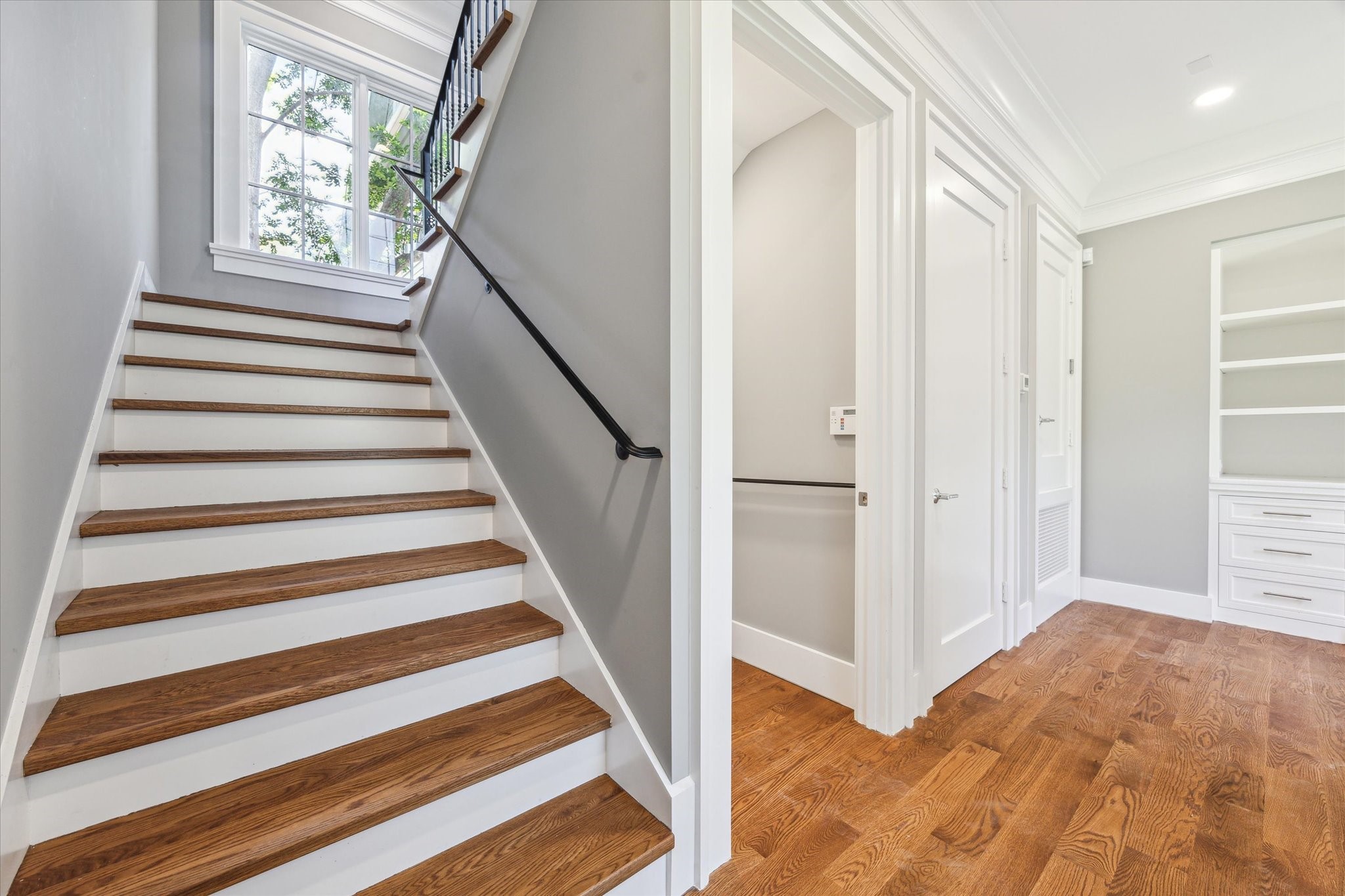 2216 Tangley Street Houston, TX 77005 - Photo 9 of 44 This photo showcases the modern, bright hallway with elegant hardwood flooring and a staircase featuring wooden treads and white risers. The door is to the elevator ready closet. The space is well-lit with natural light.