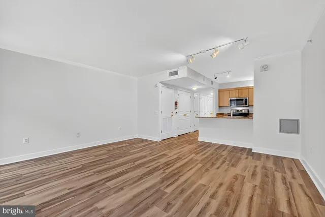 a view of empty room with wooden floor and kitchen view