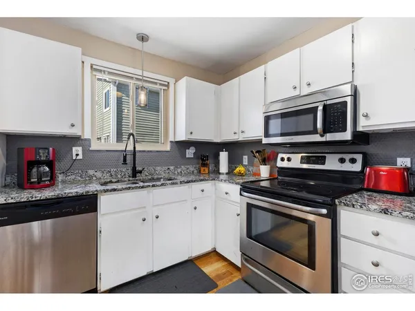 a kitchen with granite countertop a sink cabinets stainless steel appliances and a window