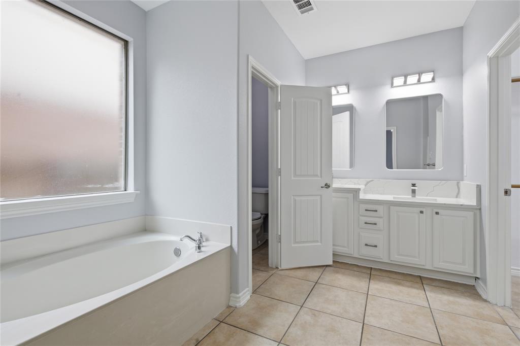 10001 Thurman Road Fort Worth, TX 76244 - Photo 19 of 40 Bathroom featuring a built-in tub with chrome fixtures, a frosted window, dual vanity with white cabinetry and integrated sinks, and neutral-toned tiled flooring