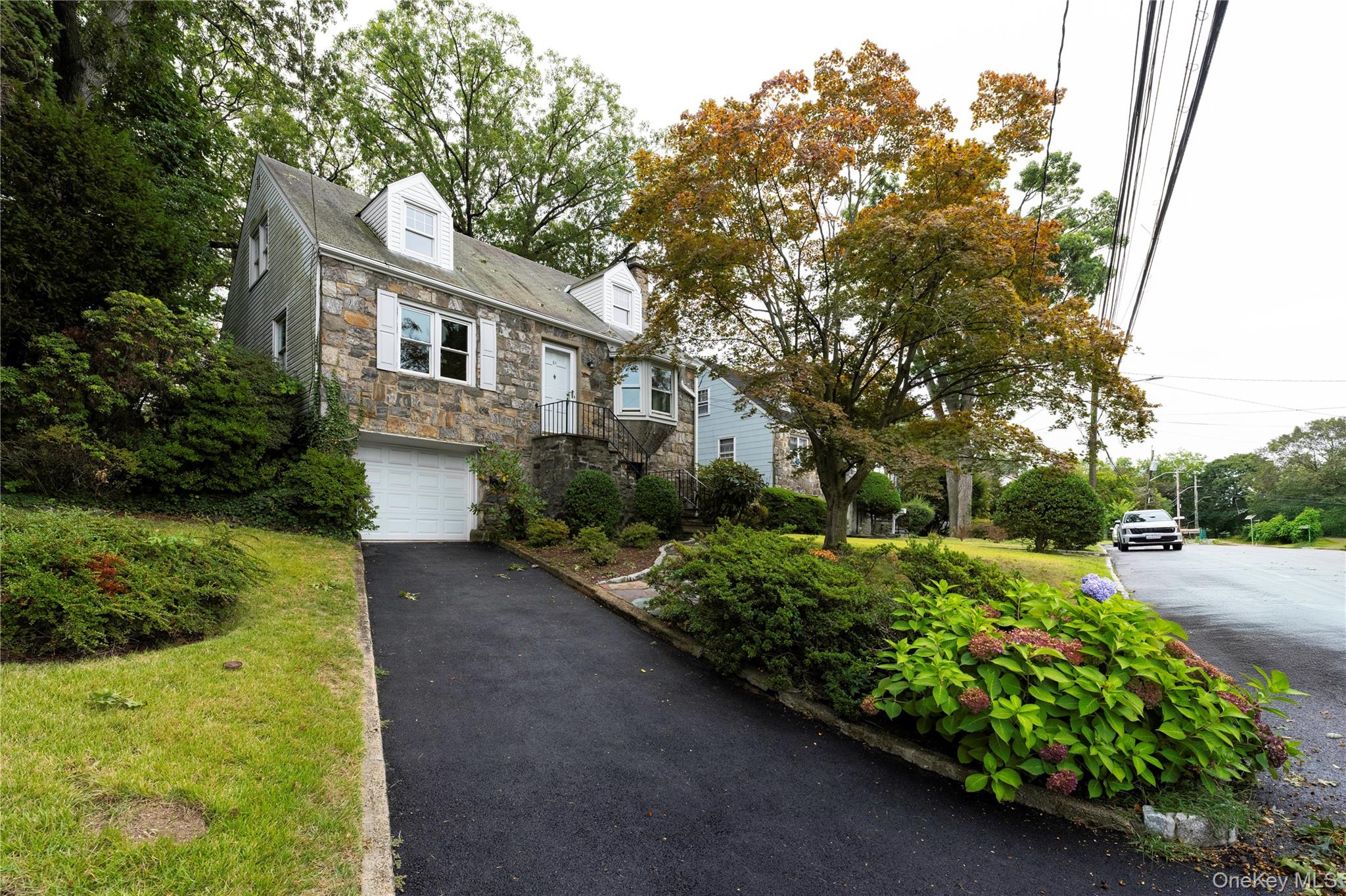 Cape cod house featuring stone siding, an attached garage, and driveway