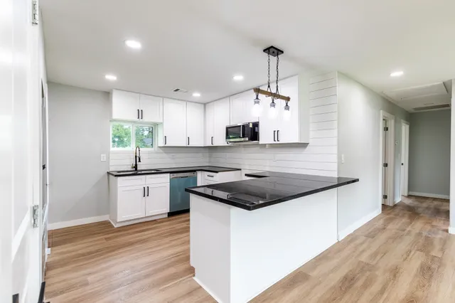 a kitchen with a stove a sink a refrigerator and white cabinets with wooden floor
