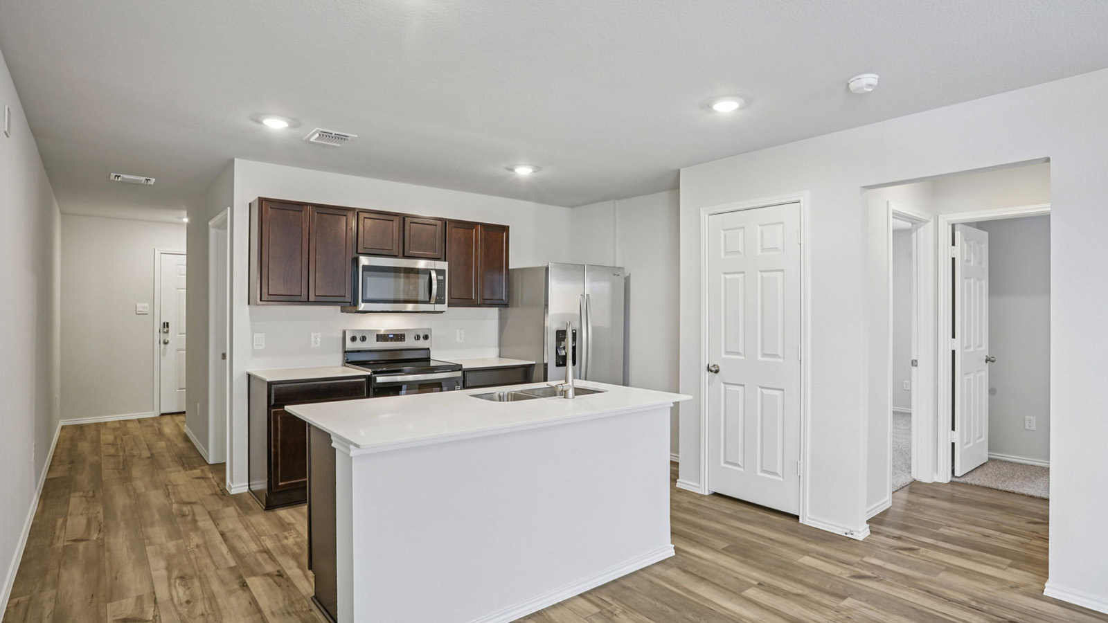 156 Wyatt Way Jarrell, TX 76537 - Photo 2 of 30 Open-concept kitchen featuring an island with counter seating, stainless steel appliances, dark wood-finish cabinetry, light countertops, and wood-finish flooring