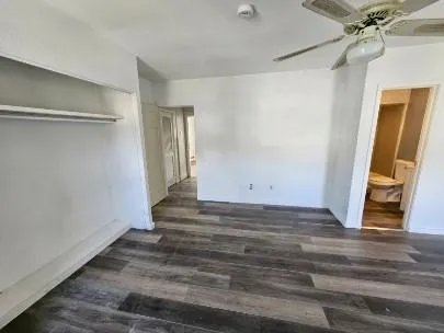 a view of an empty room with wooden floor and a ceiling fan