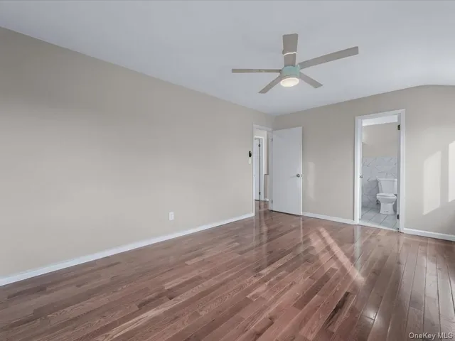 a view of an empty room with wooden floor and a ceiling fan