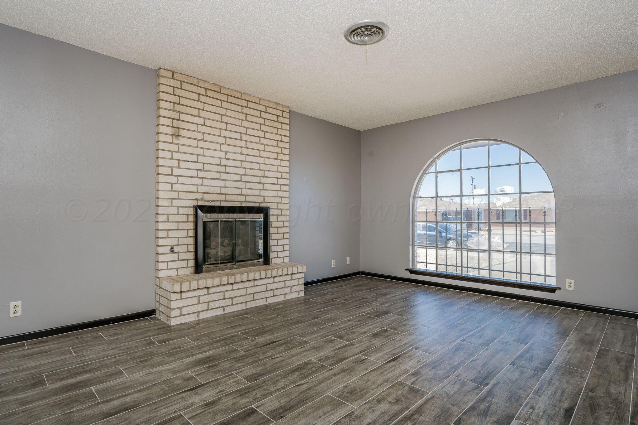 1909 Howard Drive Amarillo, TX 79106 - Photo 4 of 19 an empty room with wooden floor a fireplace and windows
