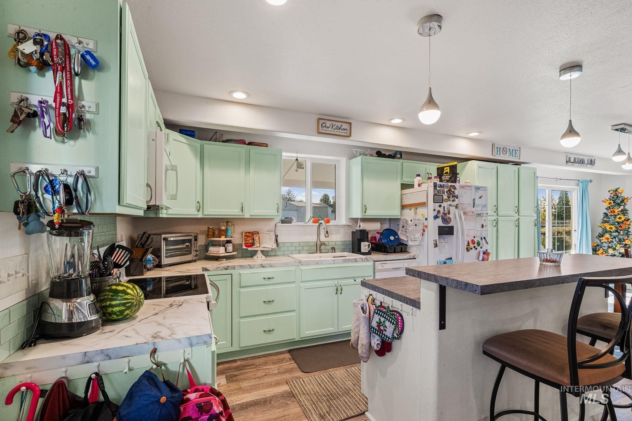 905 Fountain Street Colton, WA 99113 - Photo 11 of 34 Recessed lighting and pendant fixtures illuminate a kitchen with mint green cabinetry, white countertops, and a subway tile backsplash