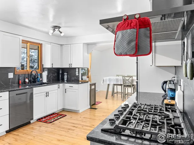 a kitchen with stainless steel appliances granite countertop a stove top oven a sink a dining table and chairs with wooden floor