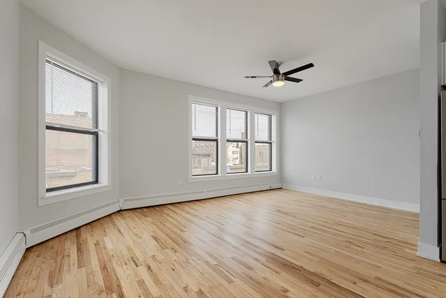 an empty room with wooden floor ceiling fan and windows