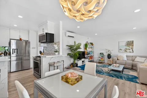 a kitchen with stainless steel appliances granite countertop a refrigerator a stove a sink a dining table and chairs with wooden floor