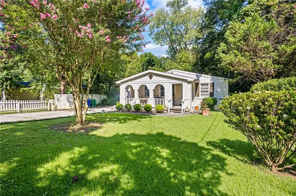 a white house with a big yard plants and large trees