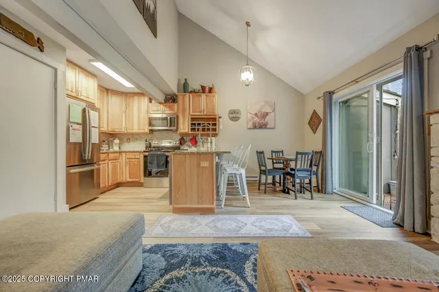 a kitchen with stainless steel appliances kitchen island granite countertop a refrigerator a stove a sink a dining table and chairs with wooden floor