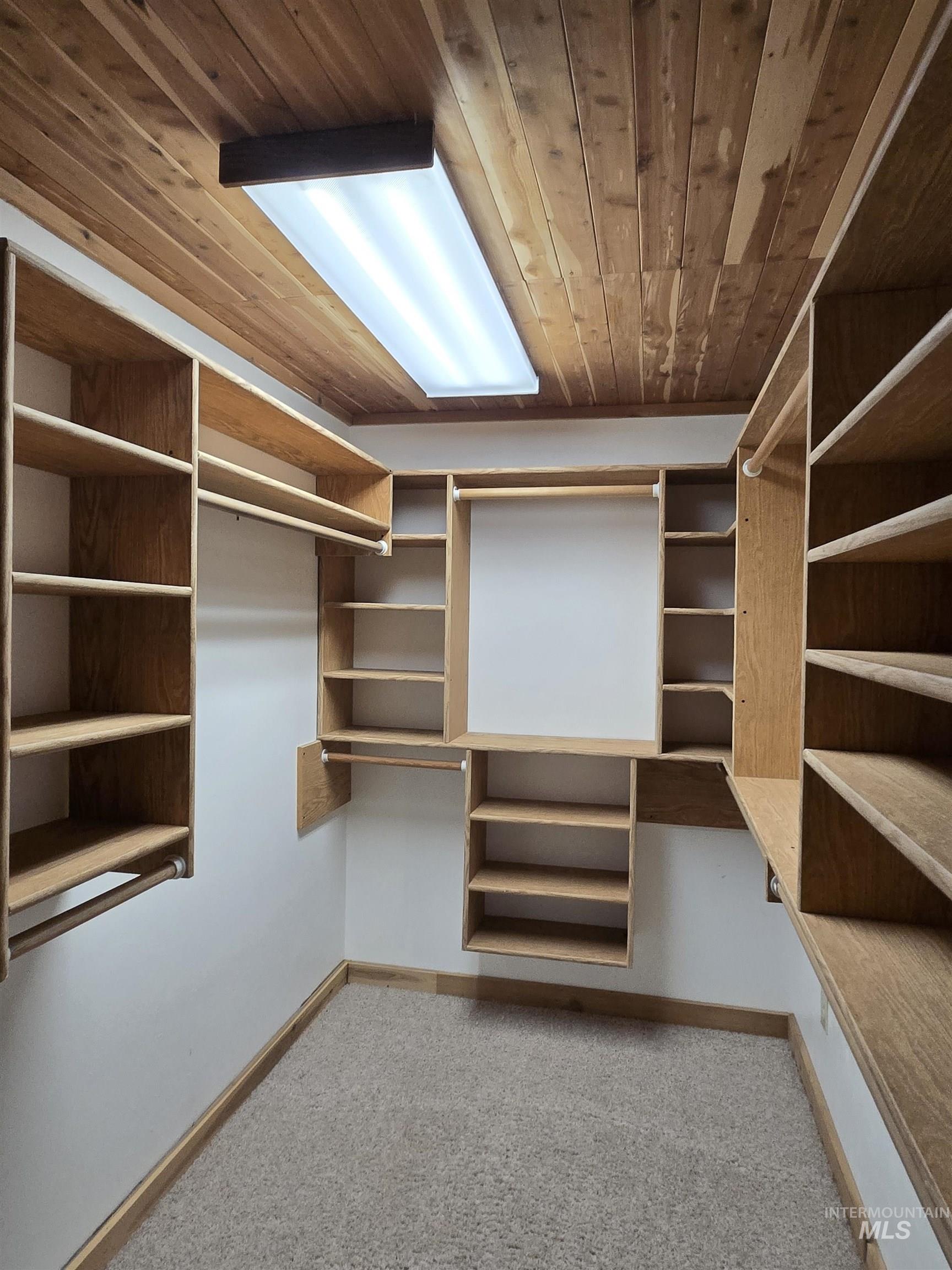12050 West Hidden Valley Rim Road Boise, ID 83709 - Photo 11 of 39 Walk-in closet featuring extensive built-in shelving, multiple hanging rods, wood-panel ceiling, carpeted flooring, and a flush-mount overhead light fixture