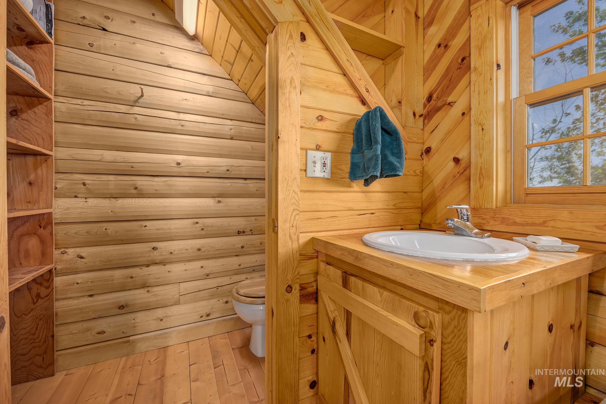 2150 Seid Creek Road Cambridge, ID 83610 - Photo 45 of 50 Natural wood-paneled bathroom featuring a window, built-in vanity with an integrated sink, chrome faucet, and wood-finish flooring