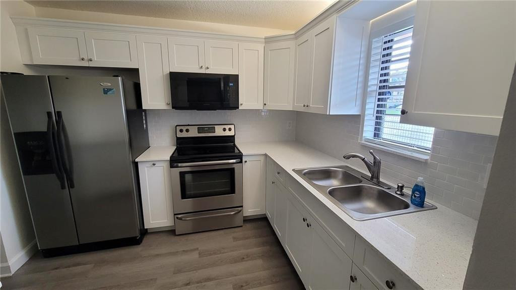 a kitchen with stainless steel appliances a sink a stove a microwave a refrigerator a window and cabinets