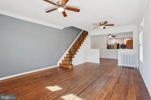 a view of an empty room with wooden floor and a ceiling fan