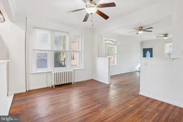 a view of an empty room with wooden floor and a ceiling fan