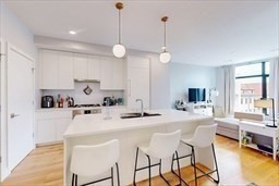 191 Washington Street, Unit 720 Boston, MA 02135 - Photo 4 of 19 a kitchen with stainless steel appliances kitchen island granite countertop a stove a sink a dining table and chairs with white cabinets
