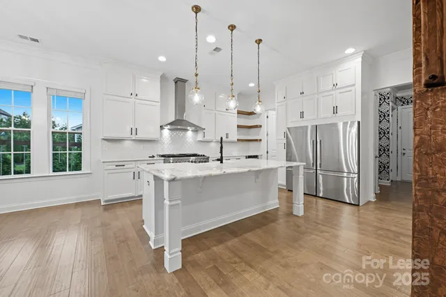 a kitchen with stainless steel appliances kitchen island granite countertop a refrigerator a stove a oven and white cabinets with wooden floor