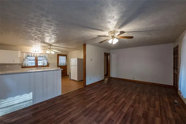 a view of an empty room with wooden floor and a ceiling fan