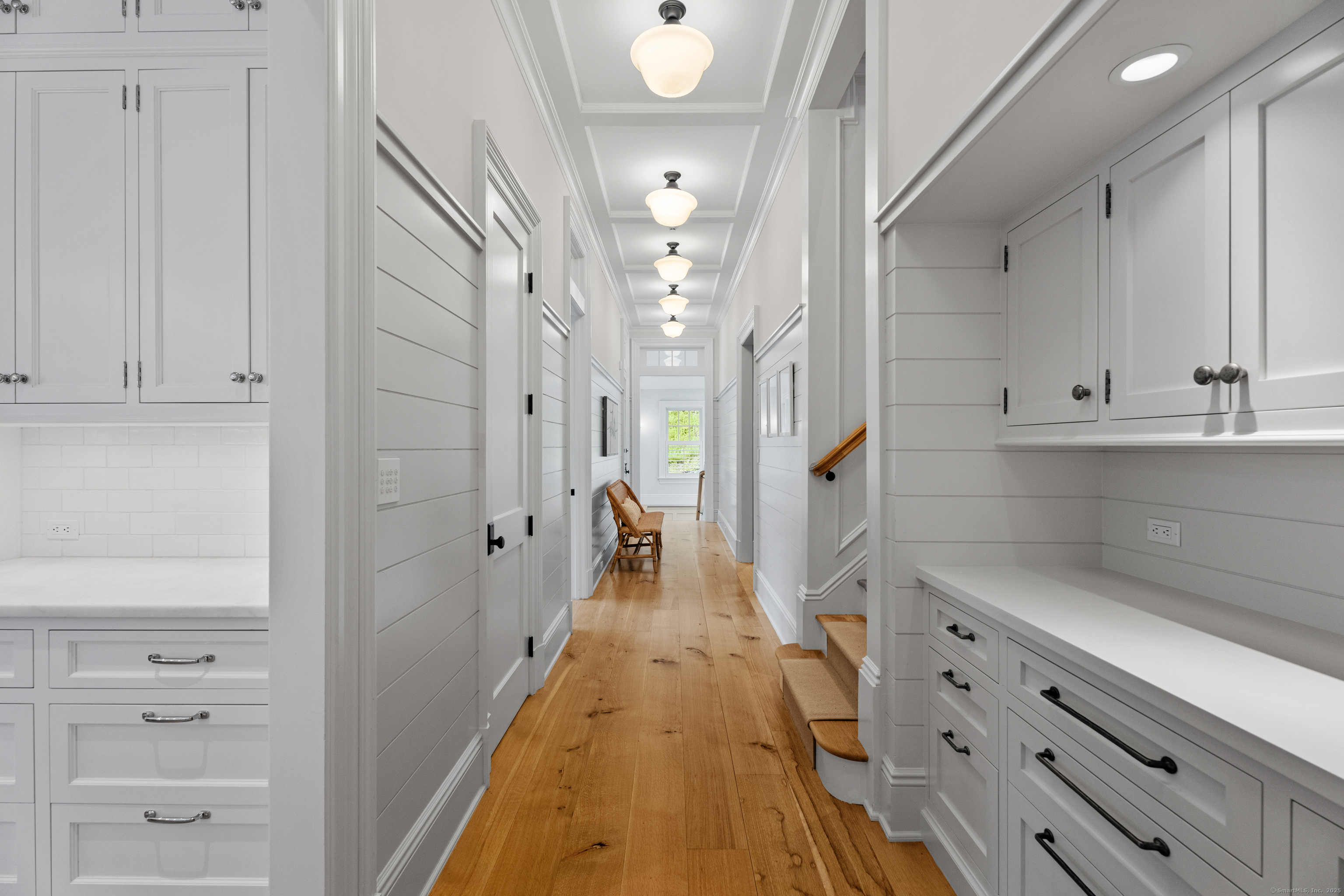 294 Maple Road Easton, CT 06612 - Photo 21 of 40 The main level hallway features an additional staircase, elegant hotel-style pendants, and custom built-ins. It offers access to the additional pantry, garage and mudroom, elevator, and bathroom, with a private entry to the lower level at the far end