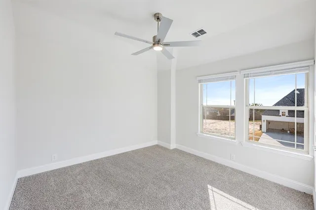 an empty room with chandelier fan and windows
