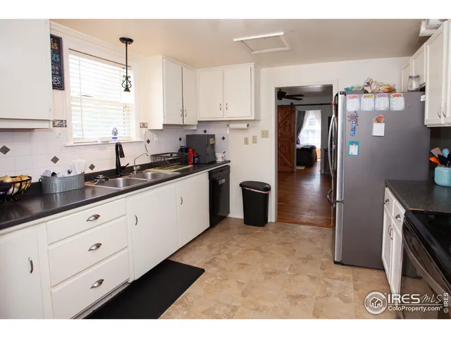a kitchen with granite countertop a refrigerator a sink and white cabinets