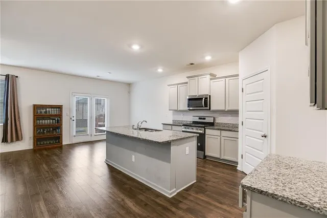 a kitchen with stainless steel appliances granite countertop a stove top oven a sink dishwasher and a refrigerator with wooden floor