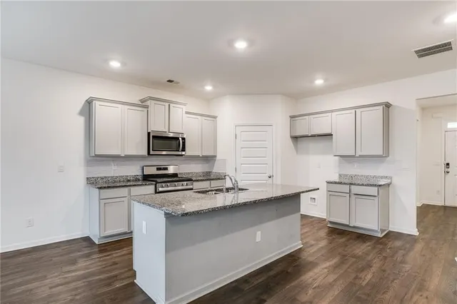 a kitchen with stainless steel appliances granite countertop a stove top oven a sink dishwasher and a refrigerator with wooden floor