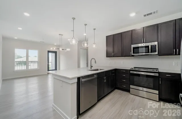 a kitchen with stainless steel appliances granite countertop wooden cabinets a sink a stove a oven and dishwasher with wooden floor