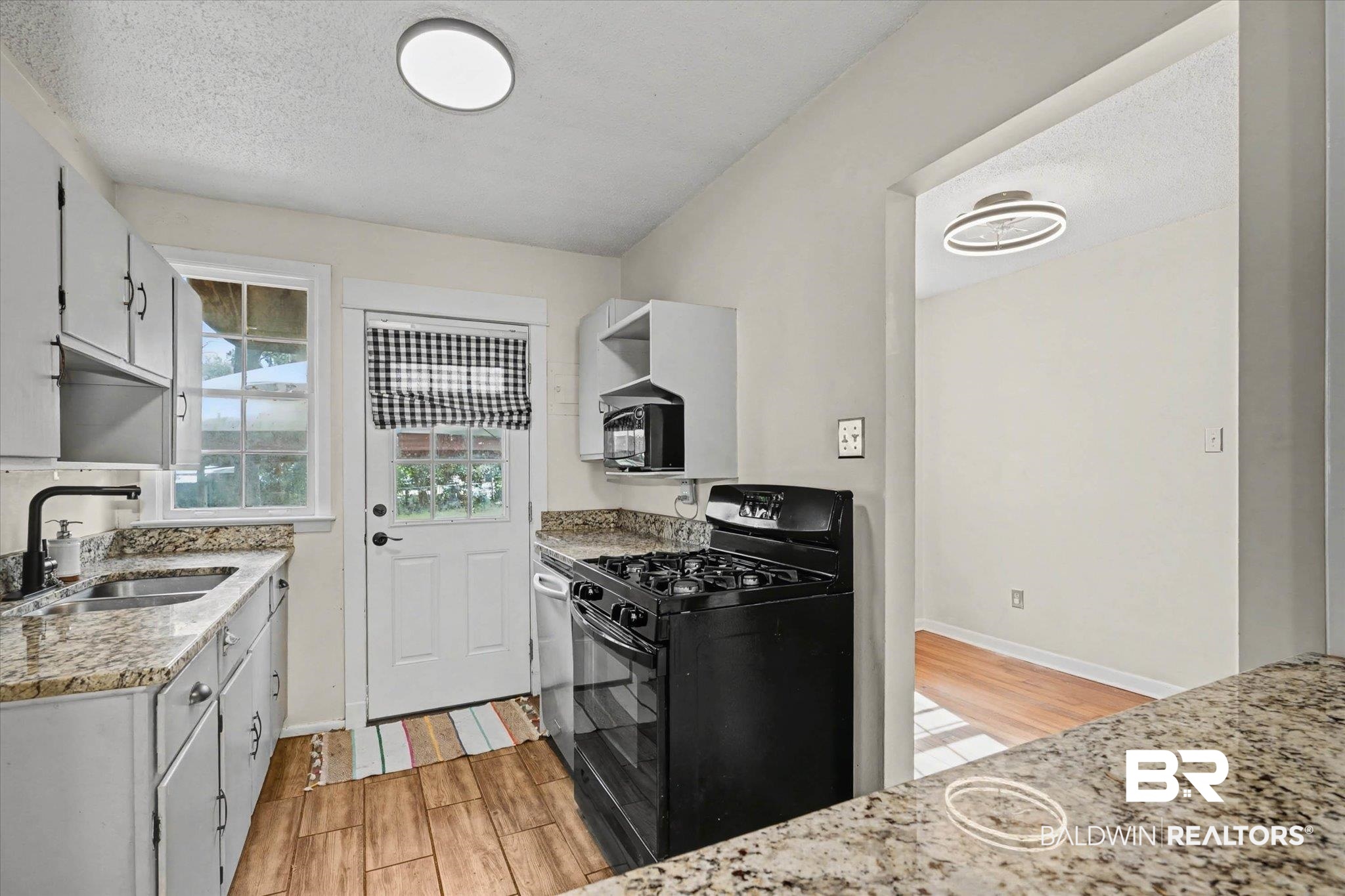5117 Norton Lane Mobile, AL 36608 - Photo 11 of 35 Kitchen with black appliances, light stone countertops, wood finish floors, a textured ceiling, and white cabinets