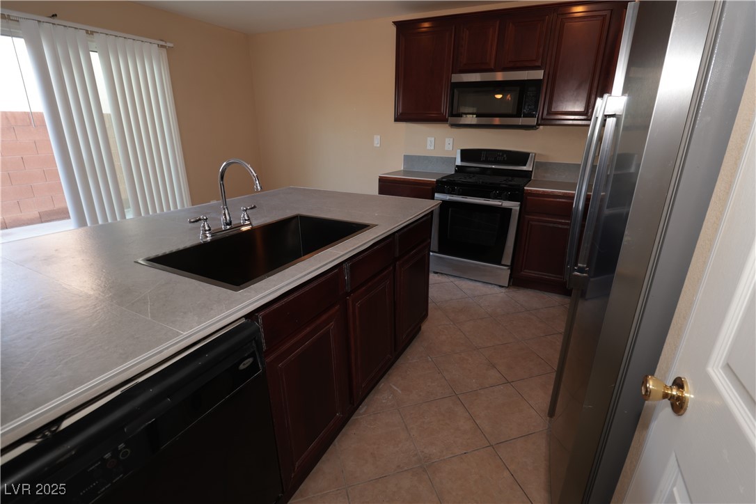 5940 Feral Garden Street North Las Vegas, NV 89031 - Photo 7 of 31 Kitchen featuring appliances with stainless steel finishes, dark brown cabinetry, light tile patterned flooring, and light countertops