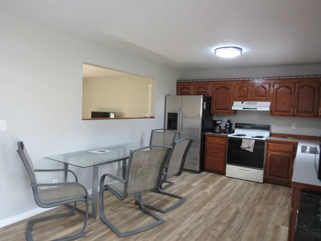 a kitchen with stainless steel appliances kitchen island granite countertop a refrigerator a stove a sink a dining table and chairs with wooden floor