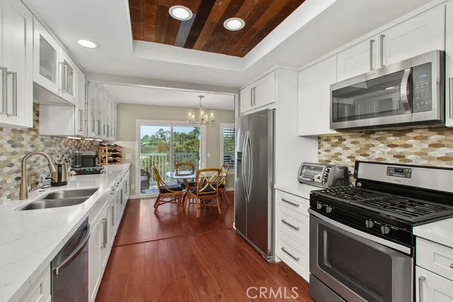 a kitchen with stainless steel appliances a stove a sink dishwasher a refrigerator white cabinets and wooden floor