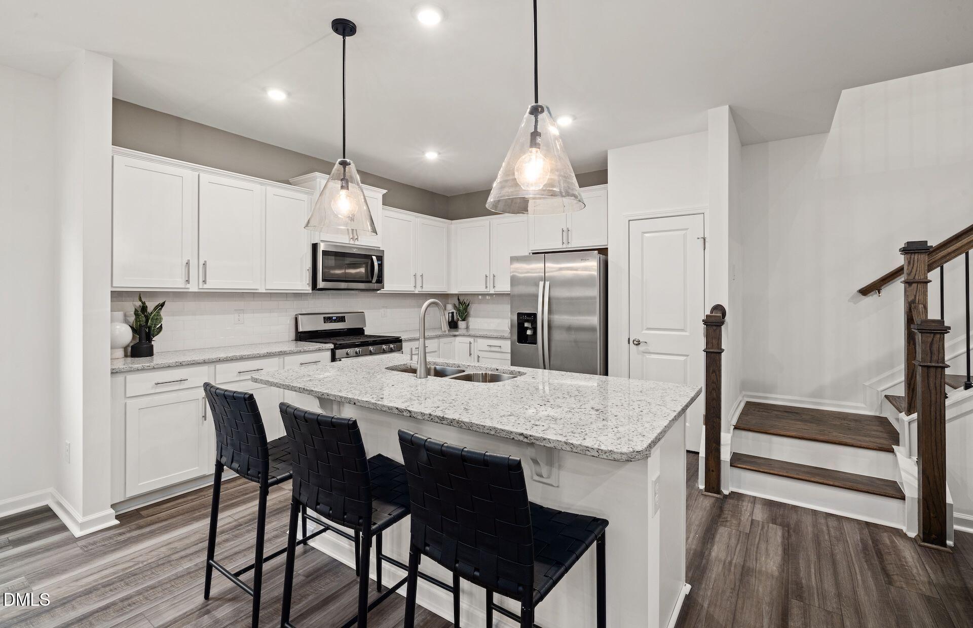 5021 Reader Way Durham, NC 27703 - Photo 4 of 32 a kitchen with stainless steel appliances granite countertop a stove a refrigerator a kitchen island a sink a stove and white cabinets with wooden floor