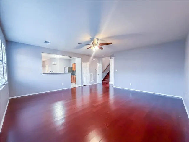 an empty room with wooden floor chandelier fan and windows