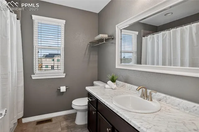 a bathroom with a granite countertop toilet a sink a mirror and a window