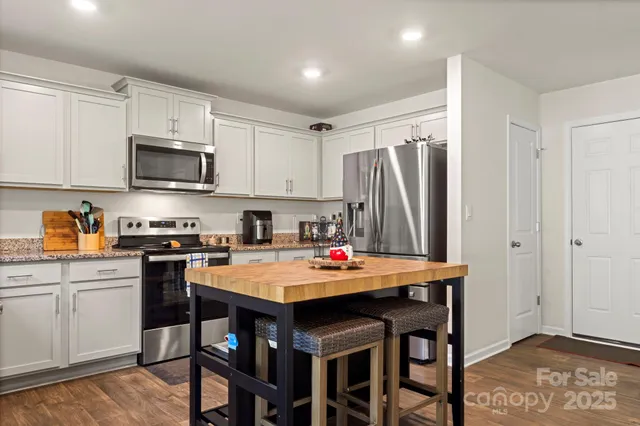 a kitchen with stainless steel appliances granite countertop a refrigerator a stove a sink a dining table and chairs