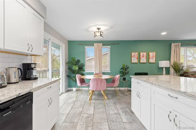 a large kitchen with granite countertop a sink white cabinets a dining table and chairs