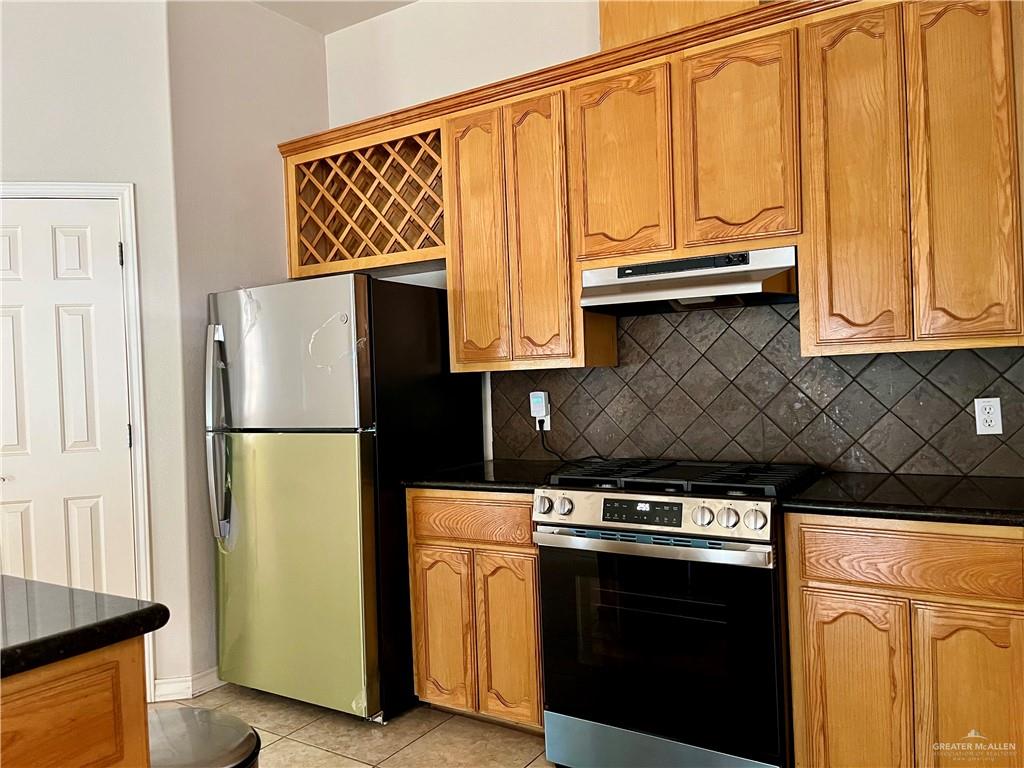 20724 North Fm 493 Road Edinburg, TX 78542 - Photo 5 of 29 Kitchen featuring under cabinet range hood, light tile patterned floors, backsplash, brown cabinets, and New appliances with stainless steel finishes