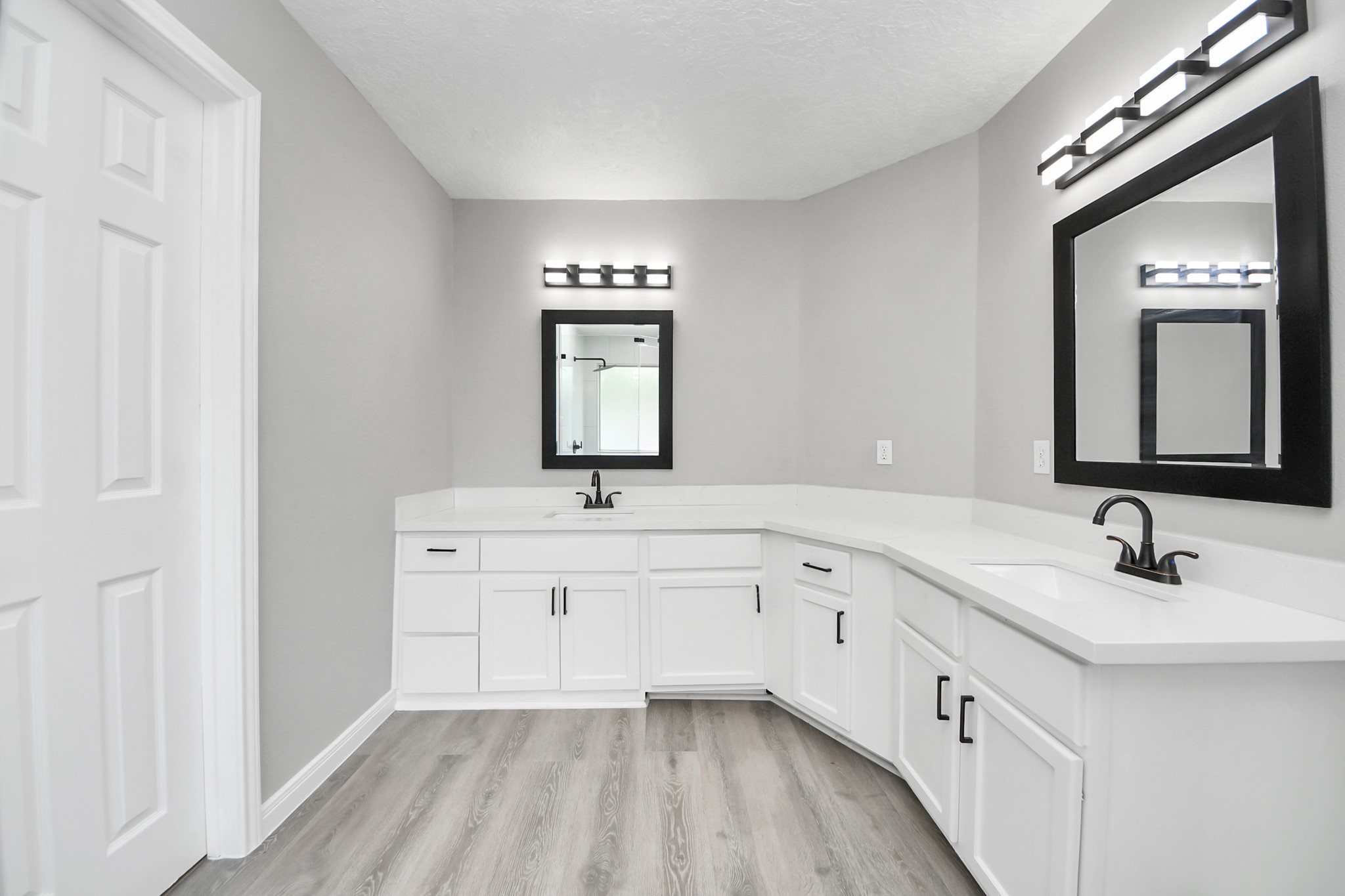 1105 East Kyle Road Clute, TX 77531 - Photo 28 of 44 The primary bathroom has dual sinks, sleek black fixtures, and white cabinetry with plenty of storage. The room is well-lit with stylish, matching mirrors, and features a neutral color palette with gray walls and light wood flooring.