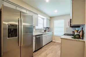 a kitchen with stainless steel appliances granite countertop a refrigerator a sink a stove and white cabinets