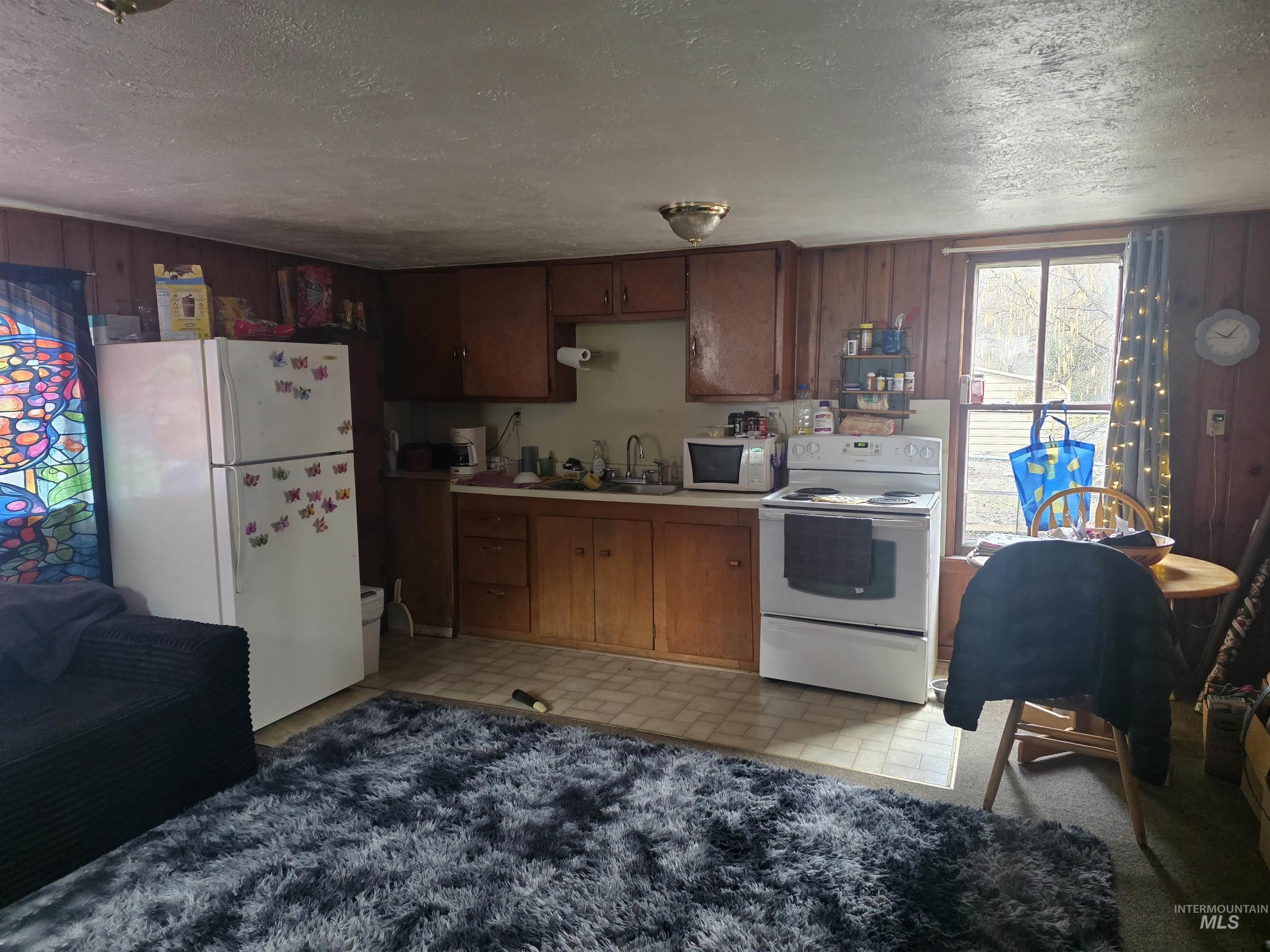 210 Pine Avenue Kooskia, ID 83539 - Photo 4 of 8 Kitchen with white appliances, a textured ceiling, light countertops, wood finish cabinetry, and wooden walls