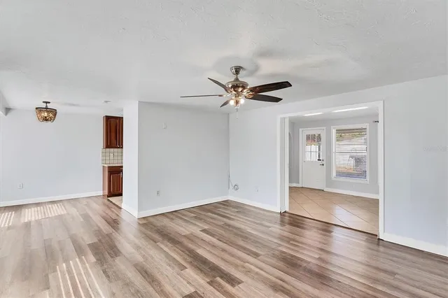 an empty room with wooden floor chandelier fan and windows