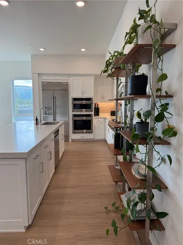 a large white kitchen with stainless steel appliances granite countertop a sink dishwasher a stove top oven a dining table and chairs with wooden floor